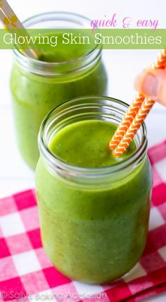 two mason jars filled with green smoothies on a checkered table cloth and straws