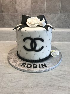 a chanel cake with white roses and black ribbon on top is sitting on a silver platter