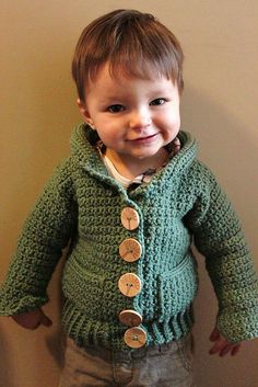 a little boy that is standing up wearing a green sweater with buttons on the front