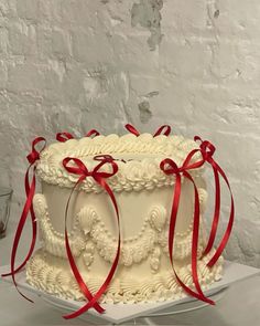 a large white cake with red ribbons on it's sides and an ornate design