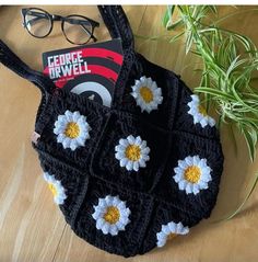 a crocheted purse with white and yellow flowers sitting on top of a wooden table