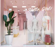 a pink and gold store front window with an angel statue in the center, surrounded by plants