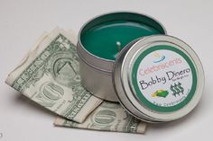 a small tin filled with money sitting on top of a white table next to a green candle