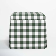 a green and white checkered ottoman cover with black piping on the bottom, sitting in front of a white wall