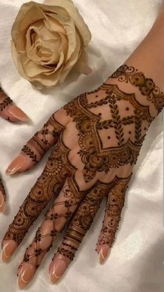 two hands with henna designs on them next to a white rose and a flower