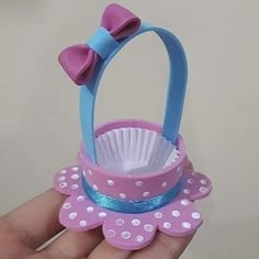 a hand holding a pink and blue cupcake shaped basket with a bow on it