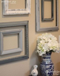 three framed pictures hang on the wall next to a vase with white flowers in it