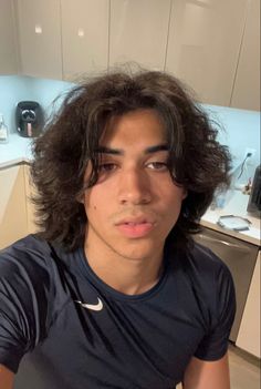 a young man with long hair sitting in a kitchen