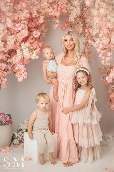 a woman and two children posing for a photo with pink flowers on the wall behind them