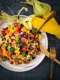 a white plate topped with salad next to corn on the cob and a fork