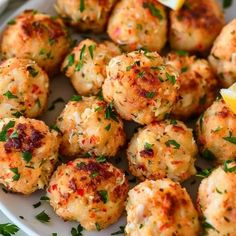 a white plate topped with crab cakes and garnished with parsley next to lemon wedges