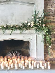 candles are lined up in front of a fireplace with flowers and greenery on the mantle