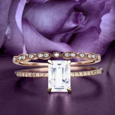 an engagement ring and wedding band with a large emerald stone in the center on a purple rose