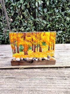 a wooden stand with rocks and trees painted on the top, sitting on a wood table