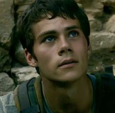 a close up of a person wearing a vest and looking off into the distance with rocks in the background