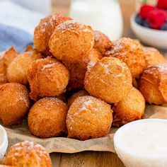 a pile of doughnuts sitting on top of a wooden table next to bowls of fruit