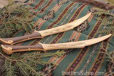 two wooden knives sitting on top of a green and red cloth next to pine branches