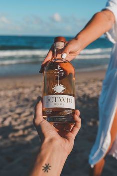 someone holding up a bottle of alcohol on the beach