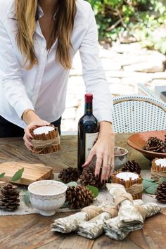 a woman is decorating pine cones on a table with wine bottle and napkins