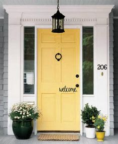 a yellow door with the words welcome on it and two potted plants next to it