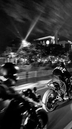 black and white photograph of motorcyclists going down the road at night time