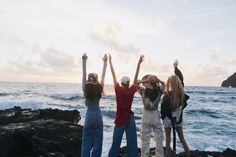 four people standing on rocks with their arms in the air