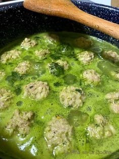 a pan filled with meatballs and broth in a green sauce next to a wooden spoon