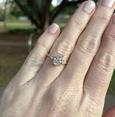 a woman's hand holding an engagement ring with two diamonds on it, in front of a tree