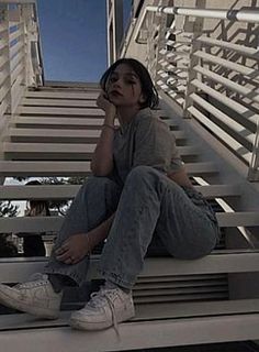 a woman sitting on top of a set of stairs next to a building with white railings