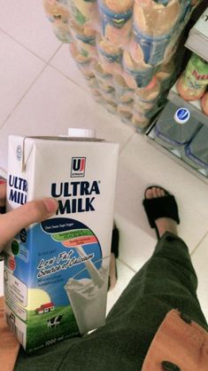 a person holding a carton of milk in front of their feet on the floor