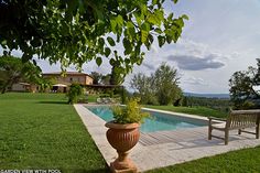 a wooden bench sitting on top of a lush green field next to a swimming pool