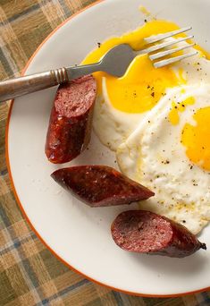 a plate with eggs, sausages and an egg on it next to a fork