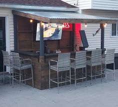 an outdoor bar with chairs and lights on the side of it in front of a house