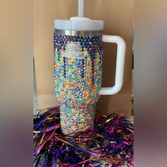 a cup filled with lots of colorful beads on top of a pile of confetti