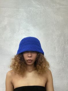 a woman wearing a blue crochet hat standing in front of a white wall