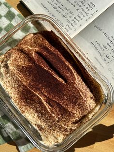 a glass container filled with food on top of a table next to an open book