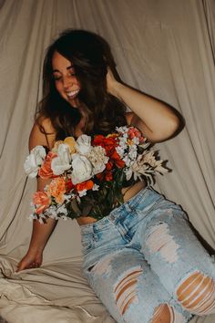 a woman sitting on top of a bed holding a bouquet of flowers in her hand