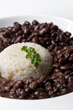 a white bowl filled with beans and rice topped with a garnished green leaf