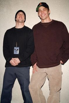 two young men standing next to each other in front of a white wall and smiling