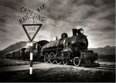 black and white photograph of an old fashioned train on the tracks with railroad crossing sign