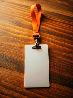 a white id card with an orange lanyard hanging from it's side on a wooden table