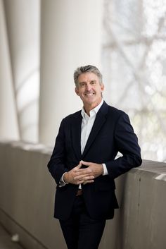 a man in a suit leaning against a wall with his hands on his chest and smiling