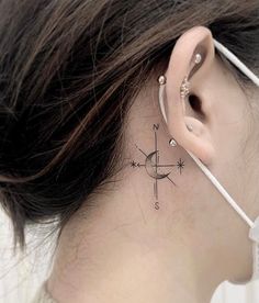 a woman's behind the ear has a compass tattoo on her left side