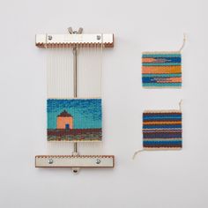 two weavings are hanging on the wall next to each other, one with a small house in it