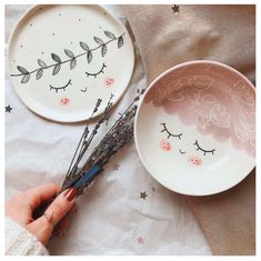 two plates with eyelashes painted on them next to a person's hand holding twig