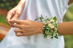 a woman wearing a white dress and holding a bouquet of flowers on her wrist with both hands