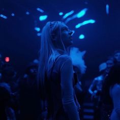 a woman with long hair standing in front of a crowd at a music concert, looking up into the sky