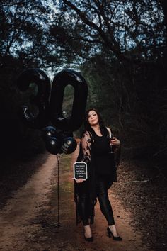 a woman standing in the middle of a dirt road holding an air filled black balloon