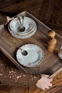 a tray with plates and silverware on top of a wooden table next to a person's hand