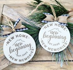 two new home ornament hanging on a wooden board with pine needles and twine